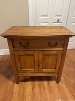 front view of wooden side table showing drawer, doors and casters
