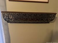 Front view of wall-mounted wood shelf with black perforated metal basket