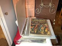 Two binders stacked, top open showing comic books in plastic sleeves