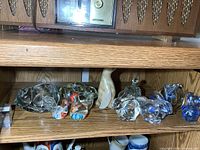 Full shelf view of glass figures, dish, rabbits, paperweight, marble bird, blue pieces