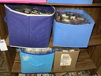Two shelves holding three fabric storage bins and a cardboard box filled with sleeved matchbooks