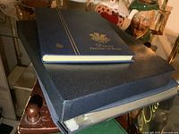 Stacked view of three stamp albums—green binder at bottom, navy binder in middle, blue Princess Diana album on top