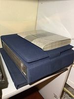 Three closed stamp albums stacked, two navy slip-cased binders and one patterned cream album