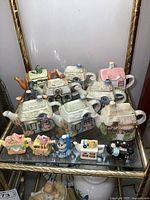 Group of cottage-shaped and miniature novelty teapots on glass shelf