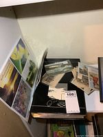 Black binder album with postcards plus stack of loose sleeved postcards on shelf