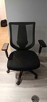 Front view of black mesh office chair with padded seat and adjustable armrests