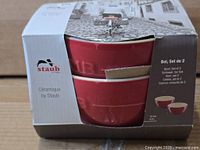 Front of packaged Staub bowl set showing two nested red bowls and branding