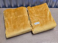 Two folded gold blackout curtain panels labeled M049