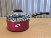 Side view of red saucepan with lid and handle