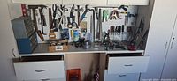 Workbench view with pegboard of hand tools, small parts cabinets, drawers