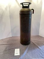 Full front view of cylindrical copper fire extinguisher with handle and outlet, showing overall form