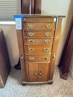 Front view of oak finish jewelry armoire showing drawers, side doors, hardware
