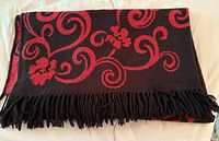 Folded throw blanket showing red floral swirl pattern on black and black fringe