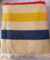 Folded wool blanket showing red, yellow, blue stripes and satin edge