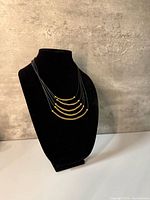Front view of necklace on bust displaying all five gold-tone brass arcs and black leather strands