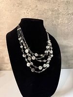 Full view of necklace on display form showing layered strands and disc charms