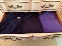 Drawer with three folded sweaters and brooch visible