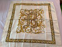 Full view of square ivory silk scarf with gold baroque border and central monogram