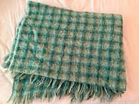 Folded green-blue plaid mohair throw showing texture and fringe