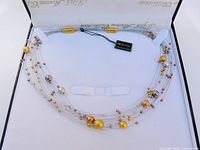 Necklace laid inside open branded box showing multi-tone beads and clasp