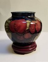 Front view of Moorcroft vase on wooden stand showing red plum motif