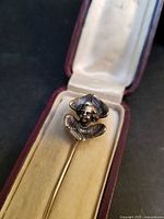 Close-up of silver angel head on gold stick pin inside box