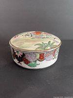 Closed round porcelain canister showing lid artwork and side decoration