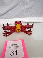 Front view of red and yellow ceramic peace frog figurine with spread limbs and peace symbol on belly
