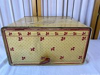 Front view of yellow Empeco bread box showing polka dot & clover pattern, red handle, overall wear