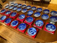 Overview of 32 blue and white Christmas plates, many in red boxes