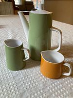 Coffee pot and two creamers standing on table