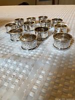 Twelve matching silver plated napkin rings displayed upright on textured white surface