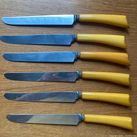 Six identical yellow-handled table knives displayed flat