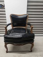 Front view of black upholstered chair with wooden frame and nailhead trim