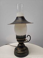 Front view of electric lamp showing base, globe, shade, chimney, and cord
