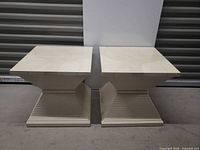 Front view of both square cream pedestal tables showing overall design