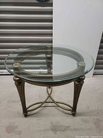 Full view of round glass side table showing metal frame and three legs