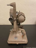 Left profile of Revere Model 85 projector showing lens, reel arm, speaker housing and power cord