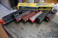 All seven model trains lined up including locomotive, five freight cars and Marx passenger car box visible