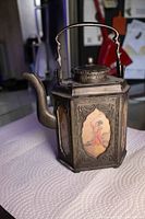 Full view of hexagonal pewter teapot showing handle, lid, spout and two painted panels