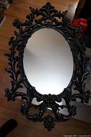 Front view of ornate black plastic framed oval mirror