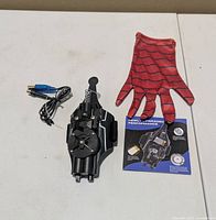 Web shooter, glove, USB cable and leaflet on tabletop