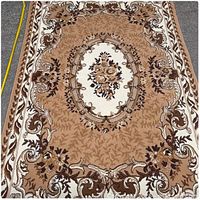 Full view of beige and brown floral area rug laid flat on pavement