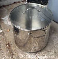 Large stainless steel stock pot with glass lid, showing side handles and interior