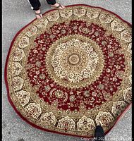 Full view of round red and beige floral rug placed on pavement, shows entire design and color scheme