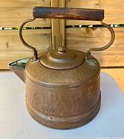 Side view of hammered copper kettle showing body, lid, handle, and spout