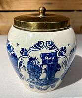 Frontal view of Delft humidor jar with brass lid showing painted tavern scene and crazed glaze