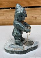 Front view of soapstone Inuit figure holding fishing line, fish on base