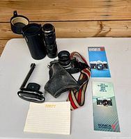 Lot overview showing camera with attached lens, zoom lens, lens case, strap, accessory bracket, manuals