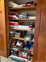 Open closet full of linens on upper shelves and craft supplies on lower shelves